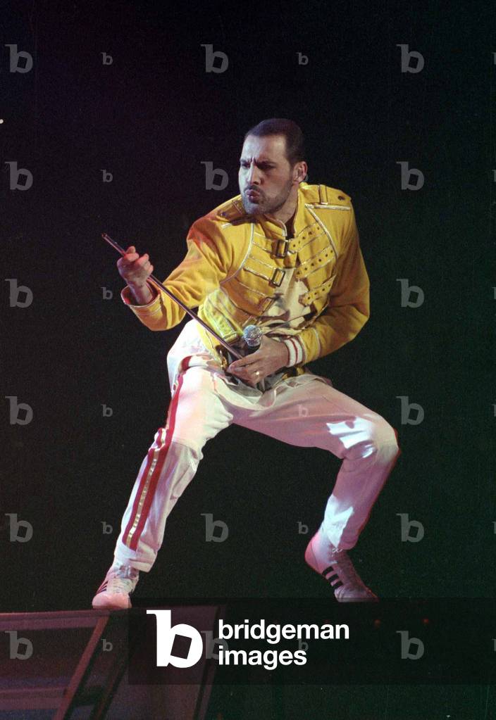 Freddie Mercury of Queen on stage during concert at Wembley Stadium, London, performing an air guitar. July 1989