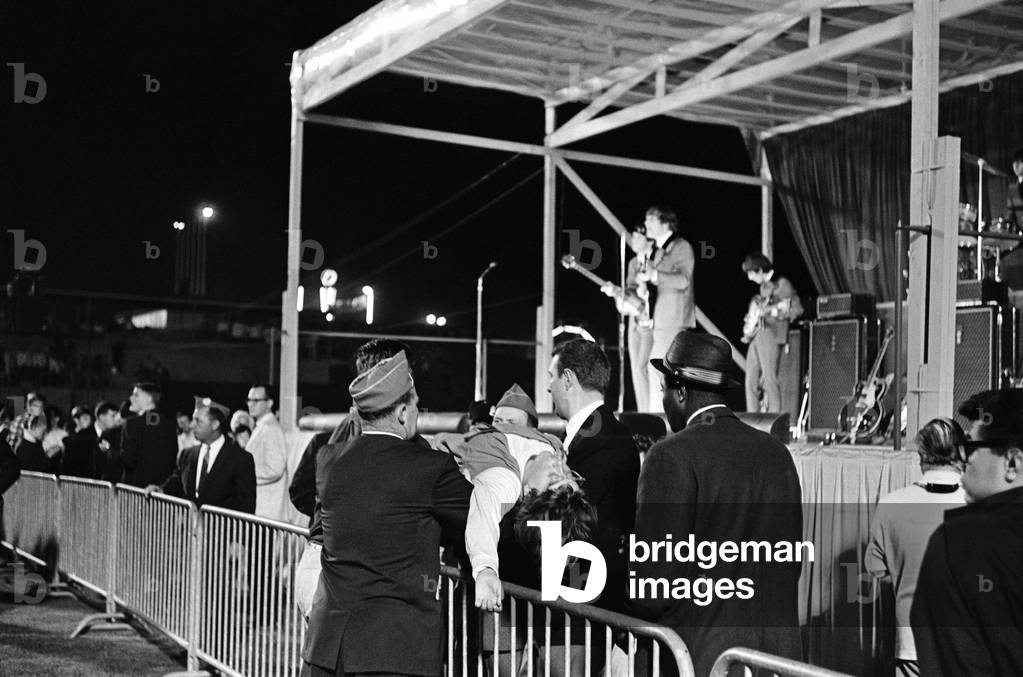 The Beatles First American Tour 19th August to 20th September 1964. The band pictured on stage at the Empire Stadium in Vancouver, British Columbia, Canada as fans are helped out. 22nd August 1964 (b/w photo)