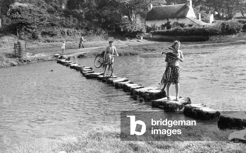A couple of young women use stepping stones to cross the Ewenny River that rises to the north east of Bridgend town, in South Wales, flows past the village of Pencoed and enters the River Ogmore estuary just below Ogmore Castle July 1943 (b/w photo)