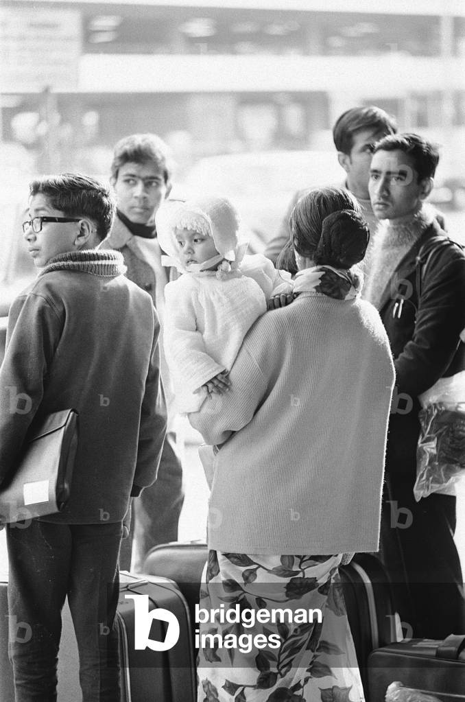 1968 East African Asian Crisis. Following Kenya achieving independence in 1963 Asians living in Kenya, were given two years to acquire Kenyan citizenship which in turn meant they had to renounce their British passports. Out of approximately 180,000 Asians fewer than 20,000 had submitted their applications by the deadline. Those Kenyan Asians without citizenship soon became subject to increasing discrimination. By 1967 the Kenyan Government enacted the Kenyan Immigration Act which required them to acquire work permits, whilst a Trade Licensing Act passed in the same year limited the areas of the country in which non-Kenyans could engage in trade. The Asian community became increasingly threatened as the Kenyan government cast them as a scapegoat group. Many choose to utilise their British passport and settle in the United Kingdom. This influx from East Africa lead the UK government to introduce The Commonwealth Immigration Act 1968 This Act took away the right of residence unless the passport holders were 'patrials' - descendents of people (parents or grandparents) born, adopted or naturalised in the UK. While the people coming from Kenya had British passports, many had not been to the UK before. The 1968 Act effectively revoked British citizenship and made thousands of people stateless. Our Picture Shows: A young Asian family arriving at Heathrow fleeing political turmoil in Kenya, waiting at the airport to be collected by friends. 27th February 1968 (b/w photo)