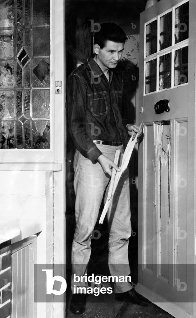 Peter Griffiths Conservative MP for Smethwick, looking at the damage to his front door which was caused by a bomb. Circa October 1965 (b/w photo)