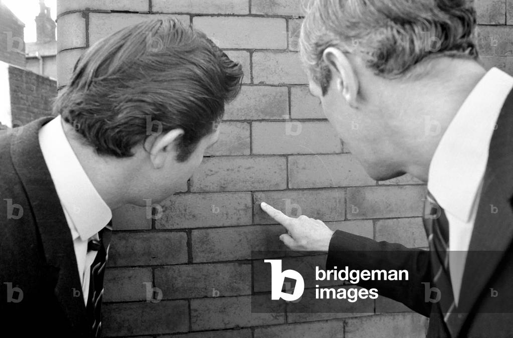 Police officer pointing out mark where bullet hit the wall, 24th January 1972 (b/w photo)