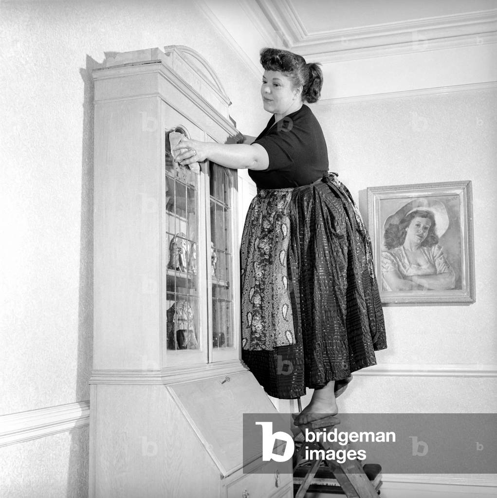 Domestic Life: Woman (Mrs. Olive Haugh) dusting the bookcase:, c. 1954 (b/w photo)