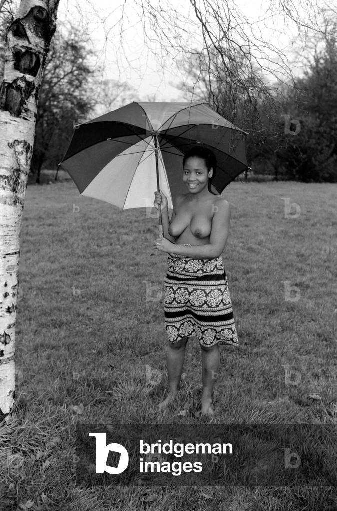 African Dancing: Ghanan Dancers. A bare-topped dancer shelter from the rain under an umbrella. December 1974