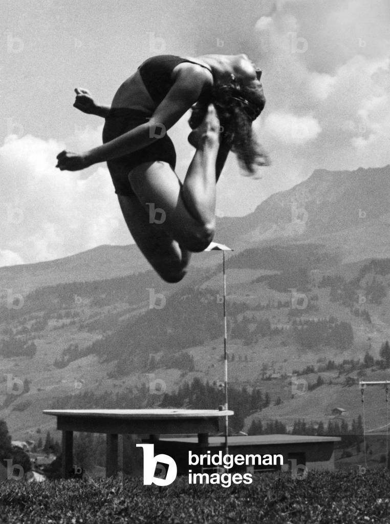 Franline Ruth Bittmann, of Basle, rhythm expert, seems to have jumped as high as the 10,000 feet mountain, wild strubel in the background of this picture taken above the famous swimming pool at Adelboden in the Berness Oberland. April 1938