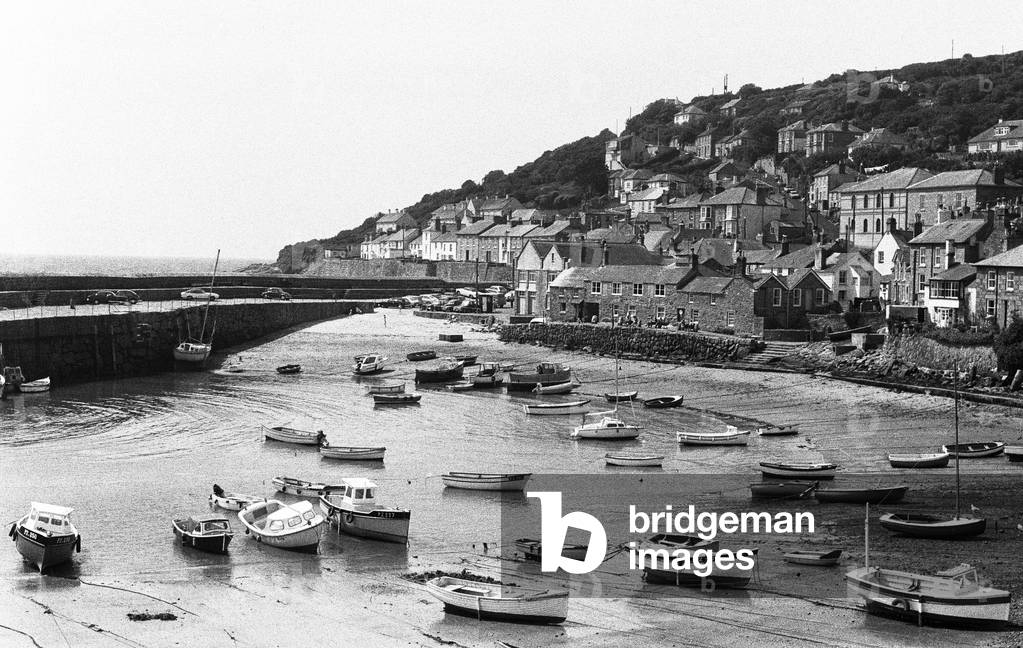 Mousehole Harbour. Mousehole is a village and fishing port in Cornwall, England. It is situated approximately 2 1ï¾¿iles (4.0 km) south of Penzance on the shore of Mount's Bay. June 1975 (b/w photo)