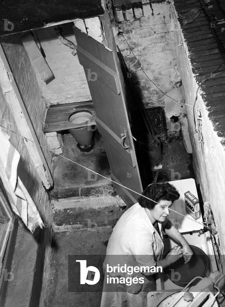 Interior view of a Liverpool terraced house showing a woman scrubbing her hands in the basin, Merseyside, 1962 (b/w photo)