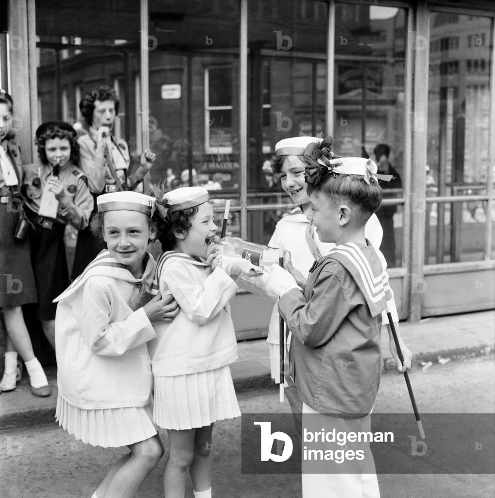 Two young friends taking part n the Manchester Whit Walks give a couple of girls a drink of water 
. June 1960
