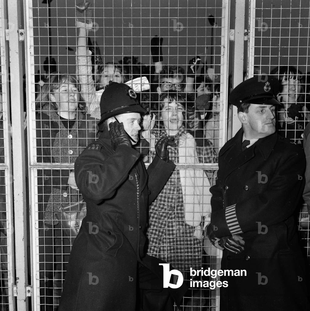 Excited female Beatles fans deafen a young policeman keeping them at bay before the concert in Sheffield, 2nd November 1963 (b/w photo)