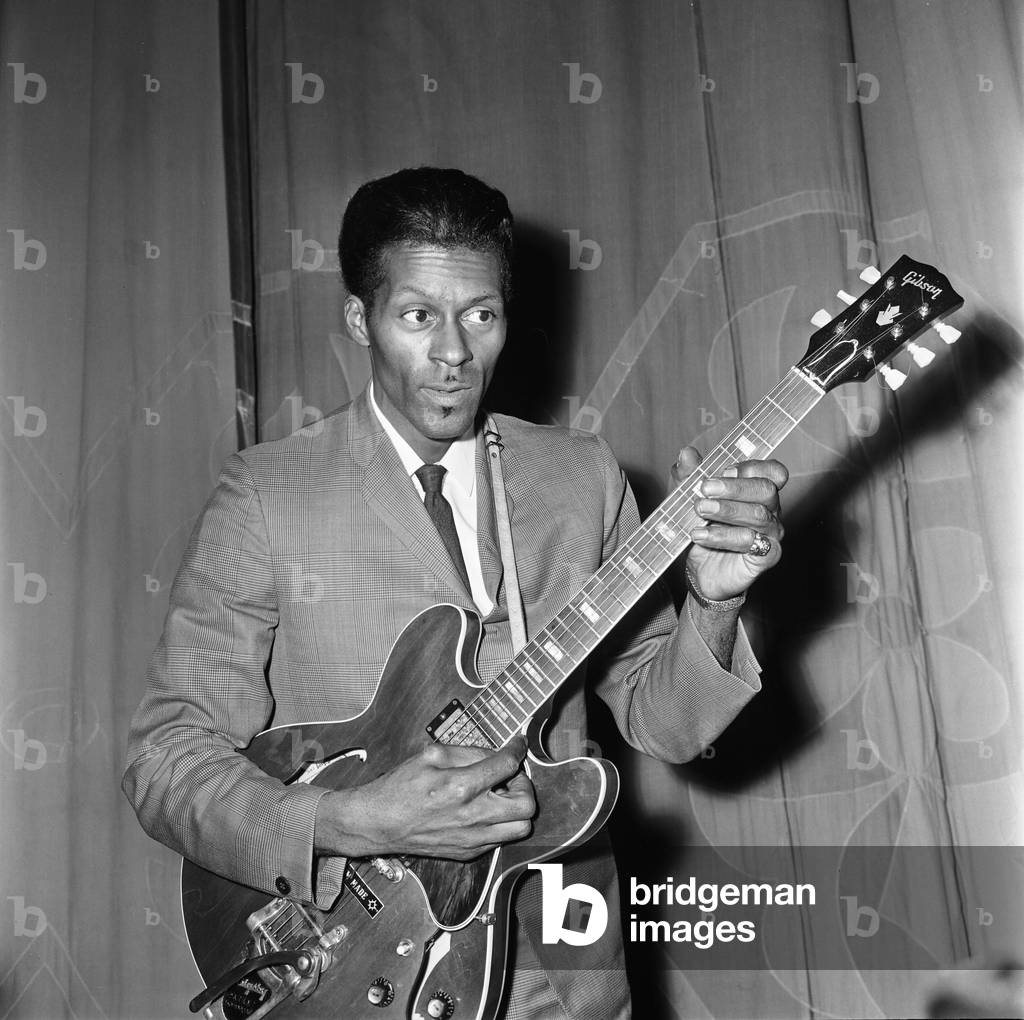 American rock and roll singer and musician Chuck Berry tunes up his guitar before going on stage to give a show at a Manchester cinema. 12th January 1965 (b/w photo)