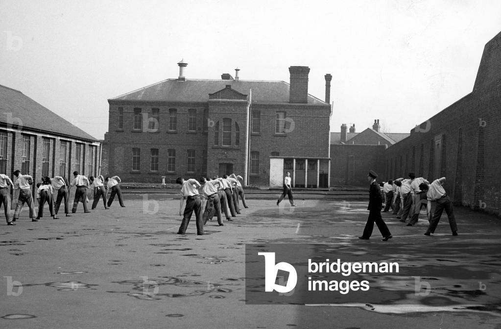 Prisoners going through their exercise routine in the yard of Durham jail watched by prison guardsApril 1956 (b/w photo)