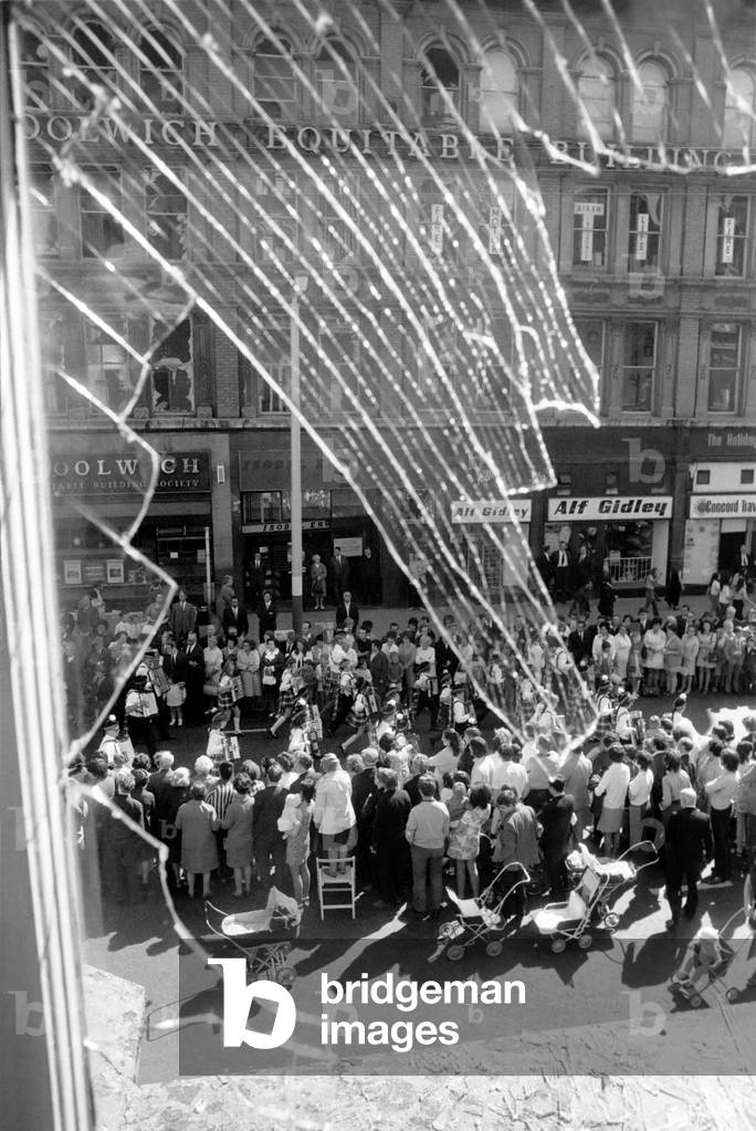 Orange Men march in Belfast. Framed in the shattered glass of a blast torn window of a Belfast Hotel, some of the 15,000 Orangemen march along Royal Avenue, Belfast. July 1971 71-6547-002