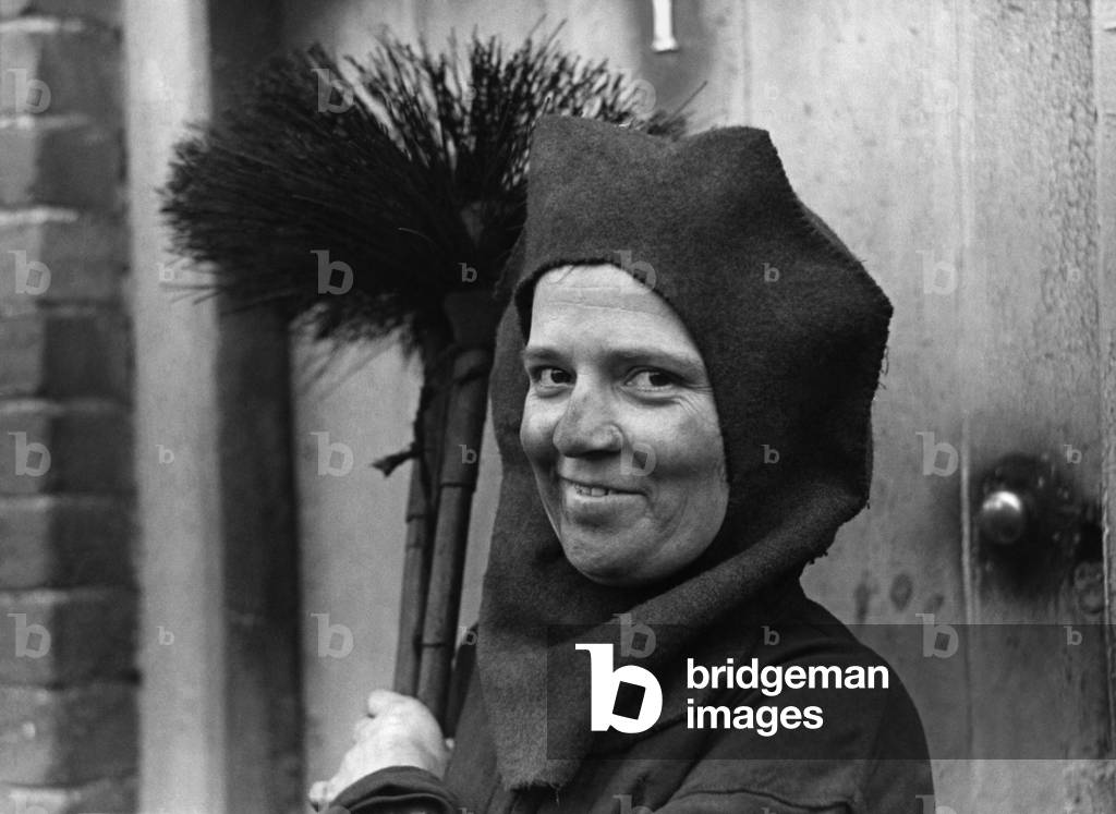 Madame Sweep: For men must work and women must sweep might be the slogan of Mrs. Ada Riches, of Woodbridge, Suffolk. She had always swept her own chimneys. Now because of the shortage of men she has become a sweep, and cleans chimneys in Woodbridge, and villages around. Mrs. Riches takes her brushes, rods, and sootbag around on a bicycle. She starts work at 7am, and by noon has cleaned ten chimneys. The head and hair protector, reminiscent of the middle ages is her own design. Photo shows... here you see Mrs. Ada Riches arriving on the job, sooty, but cheerful. October 1943 (b/w photo)