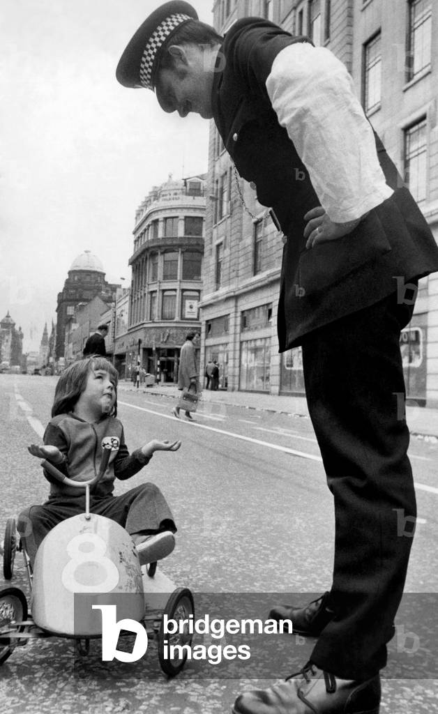 It's a fair cop for little Craig Wright as he pedals along Argyle Street. July 1976