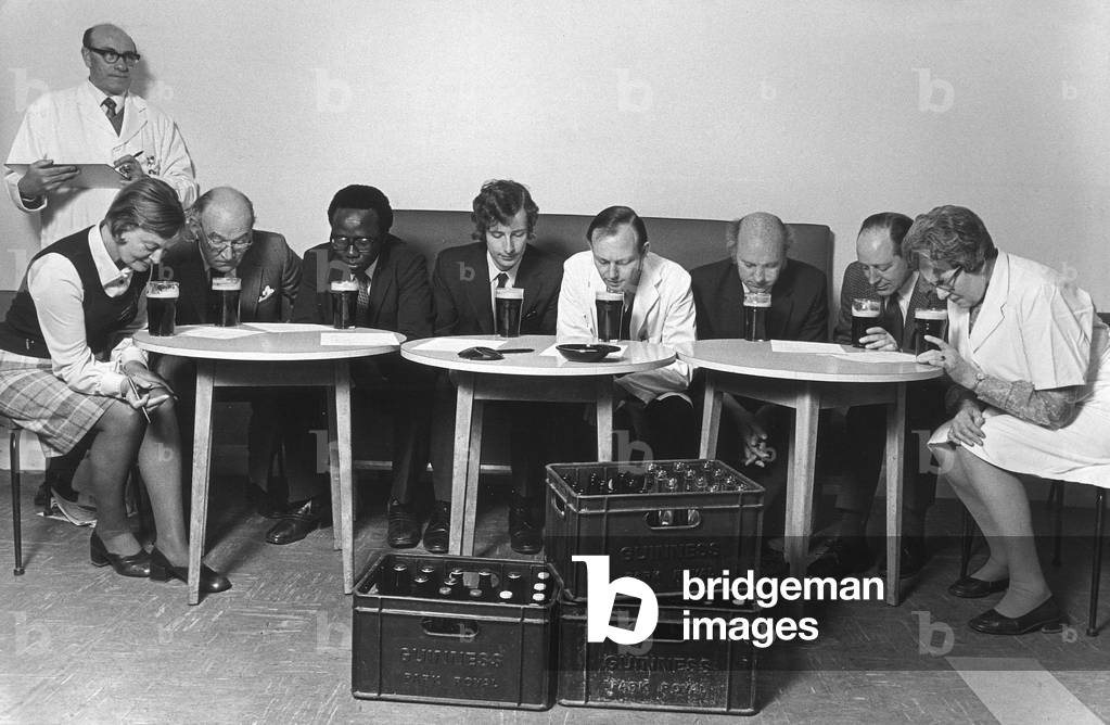 A tasting panel of men and women smell the aroma from glasses of Guinness at the Park Royal brewery sampling room, 30/05/1975 (b/w photo)