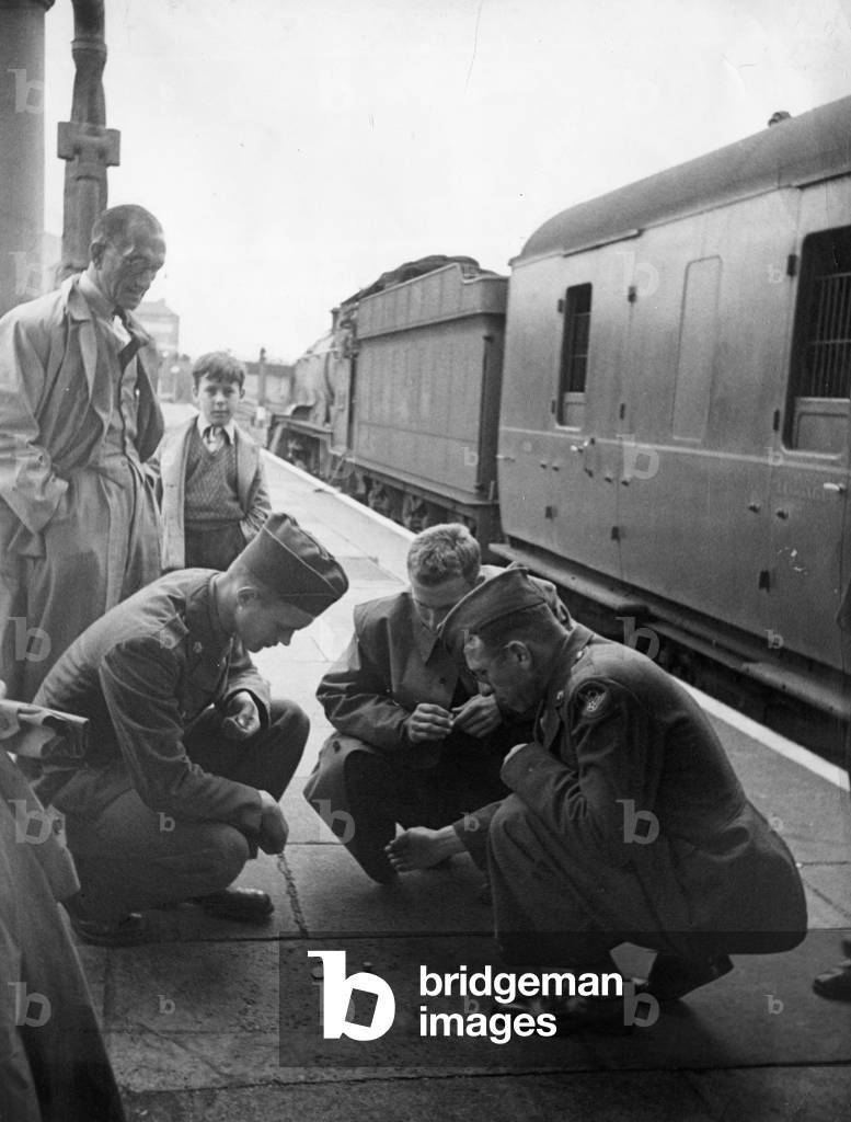 American army soldiers while away the time waiting for a train to leave, by shooting craps on the platform of a station in England during the Second World War August 1943 (b/w photo)