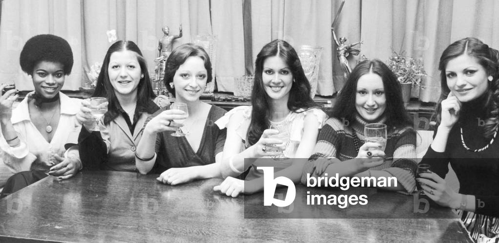 Cheers! A celebration drink for the six girls who won their way through to the finals of the Coventry Carnival Queen competition to be held at the Lord Mayors ball on April 2nd 1977 The six Coventry girls are (left to right) Beryl Clarke 17, Katrina King 19, Julie Evans 18, Susan Jago 18, Lesley Mason 21 and Prudence Porretta 21. 18th March 1977 (b/w photo)