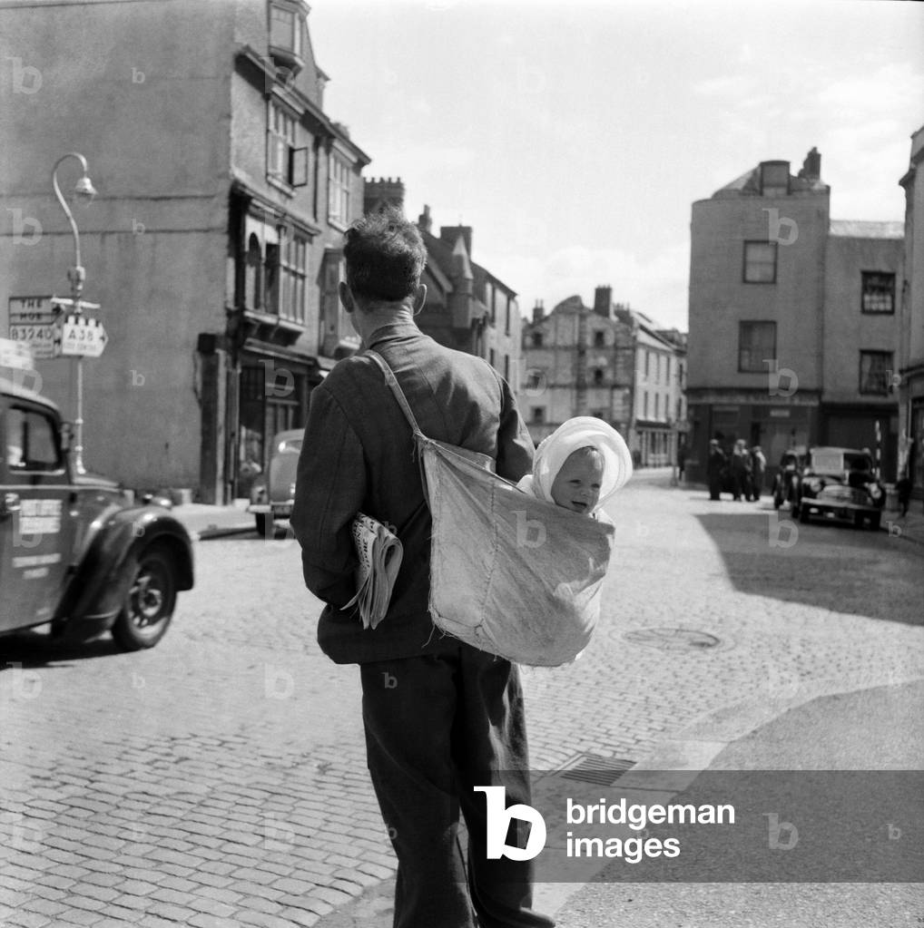 Bill Ward delivering papers and carrying baby grand daughter Jennifer Howbley. July 1953 D3535