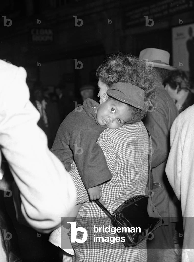 One tired little traveller gets a helping hand from his mother as they arrive at Paddington Station near the end of their journey from Jamaica to start a new life in the United Kingdom, 1st May 1955 (b/w photo)