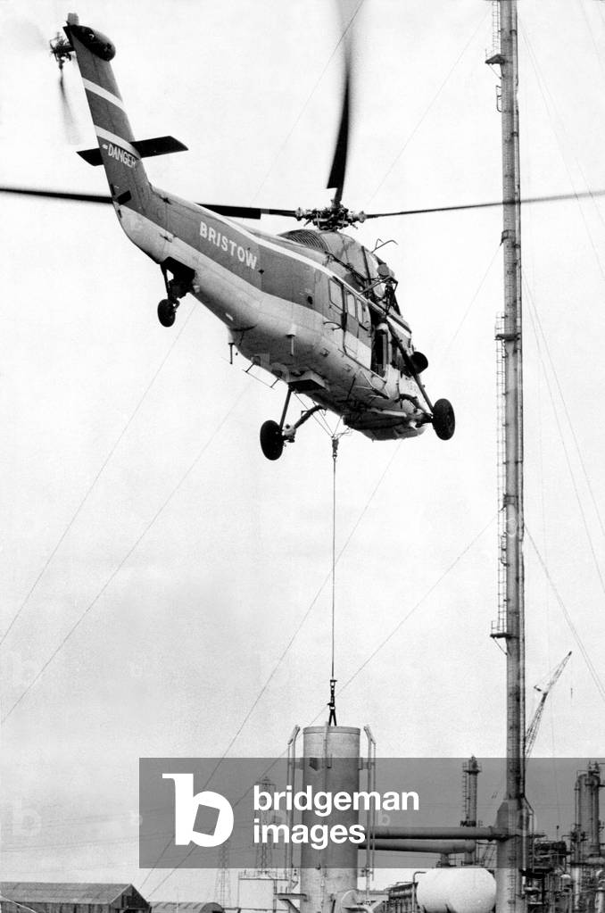 A Westland Wessex helicopter, operated by Bristow, tackles the job of airlifting the tip of a 352 ft flarestack at ICI's North Tees works, near Billingham, 23/09/1972 (b/w photo)