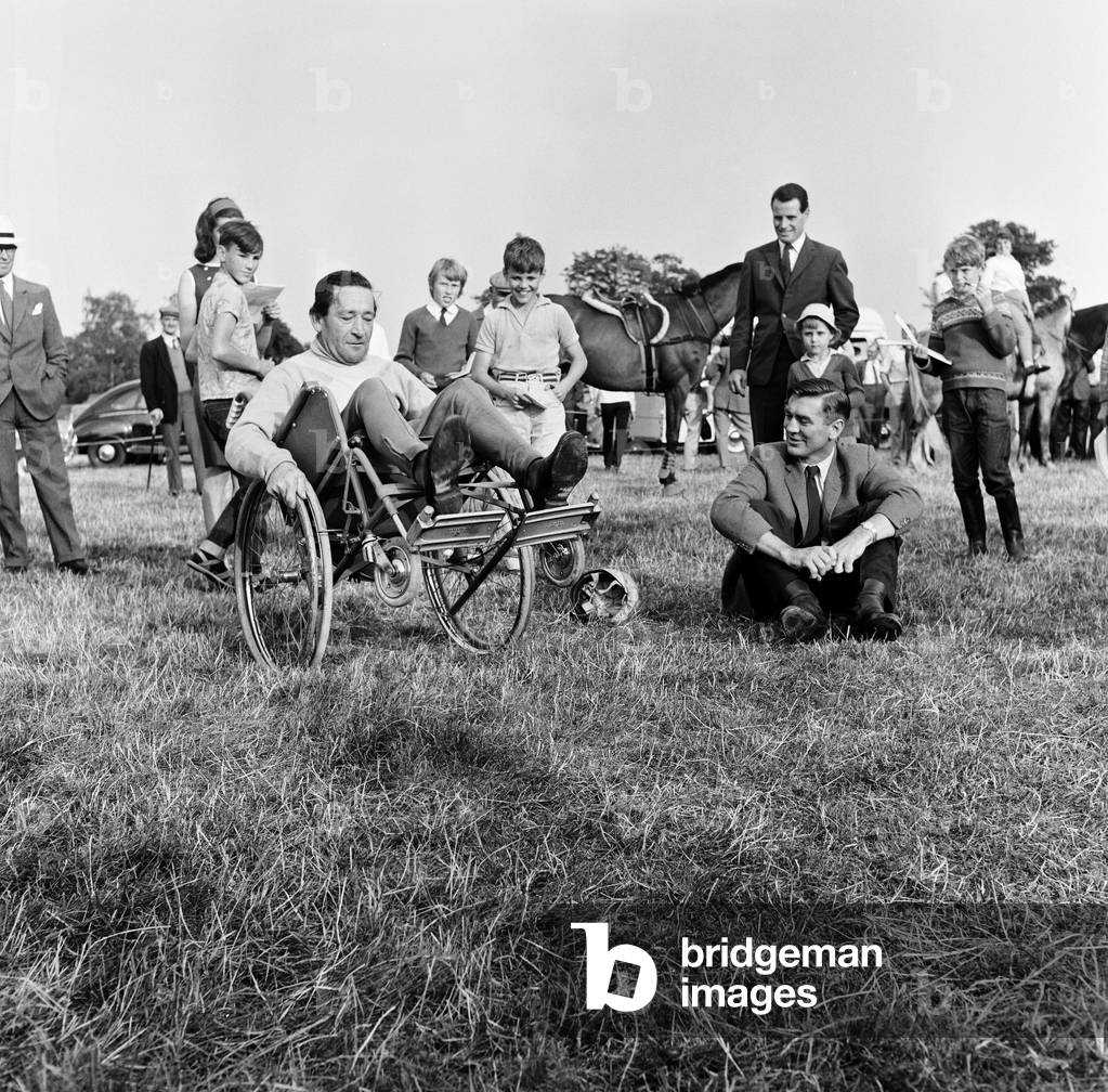 Finmere Jumping Show and Gymkhana near Buckingham in aid of Stoke Mandeville Games. Injured steeplechase jockey Tim Brookshaw shows Fred Winter a trick with his wheelchair and Fred comes to grief. 11th August 1964 (b/w photo)
