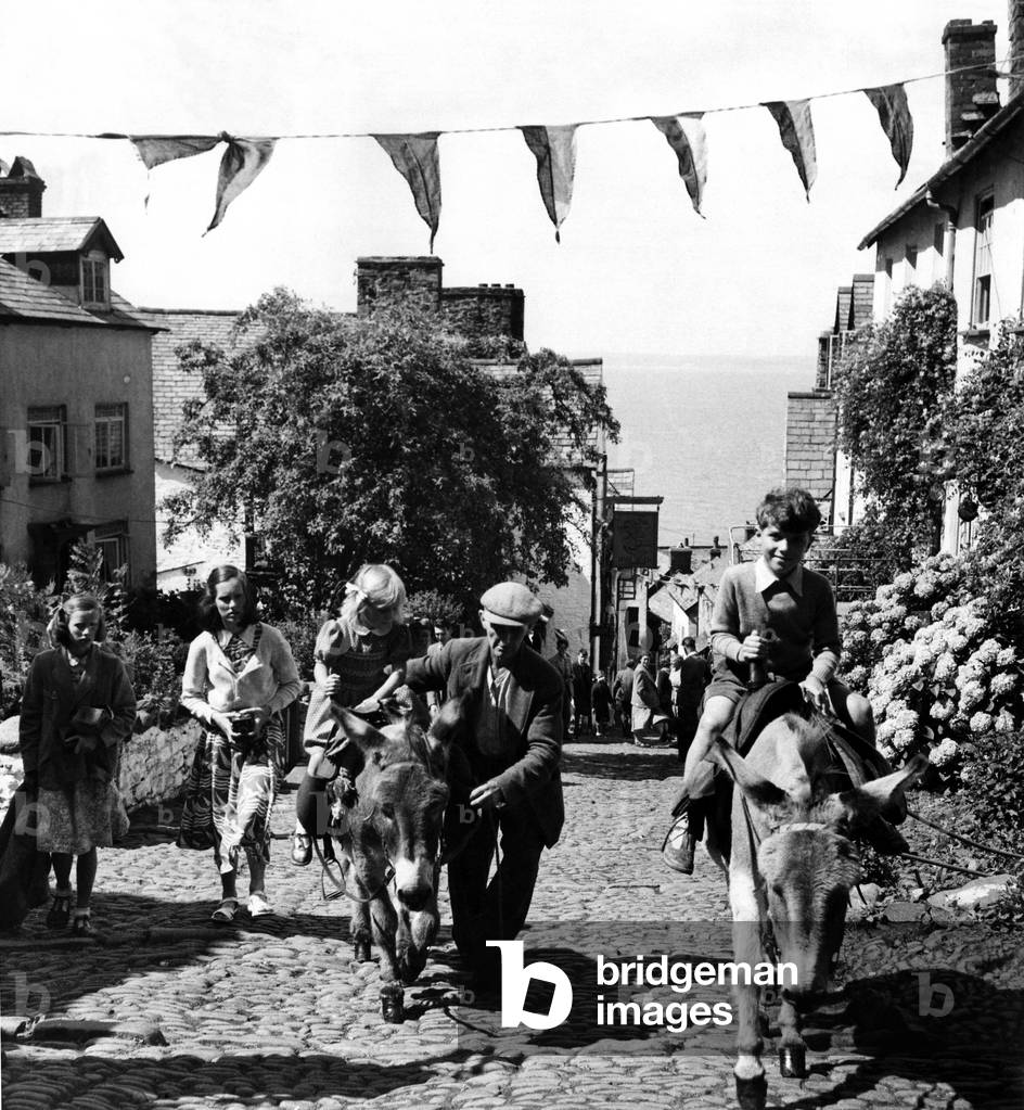 Mr. Gulliver takes a party of elderly people from the harbour of Clovelly to the top of the cliff in his jeep. The children being lighter in weight are able to enjoy a donkey ride to the top. Leading the donkeys is, deaf and dumn Earnest Beer, aged 58. 