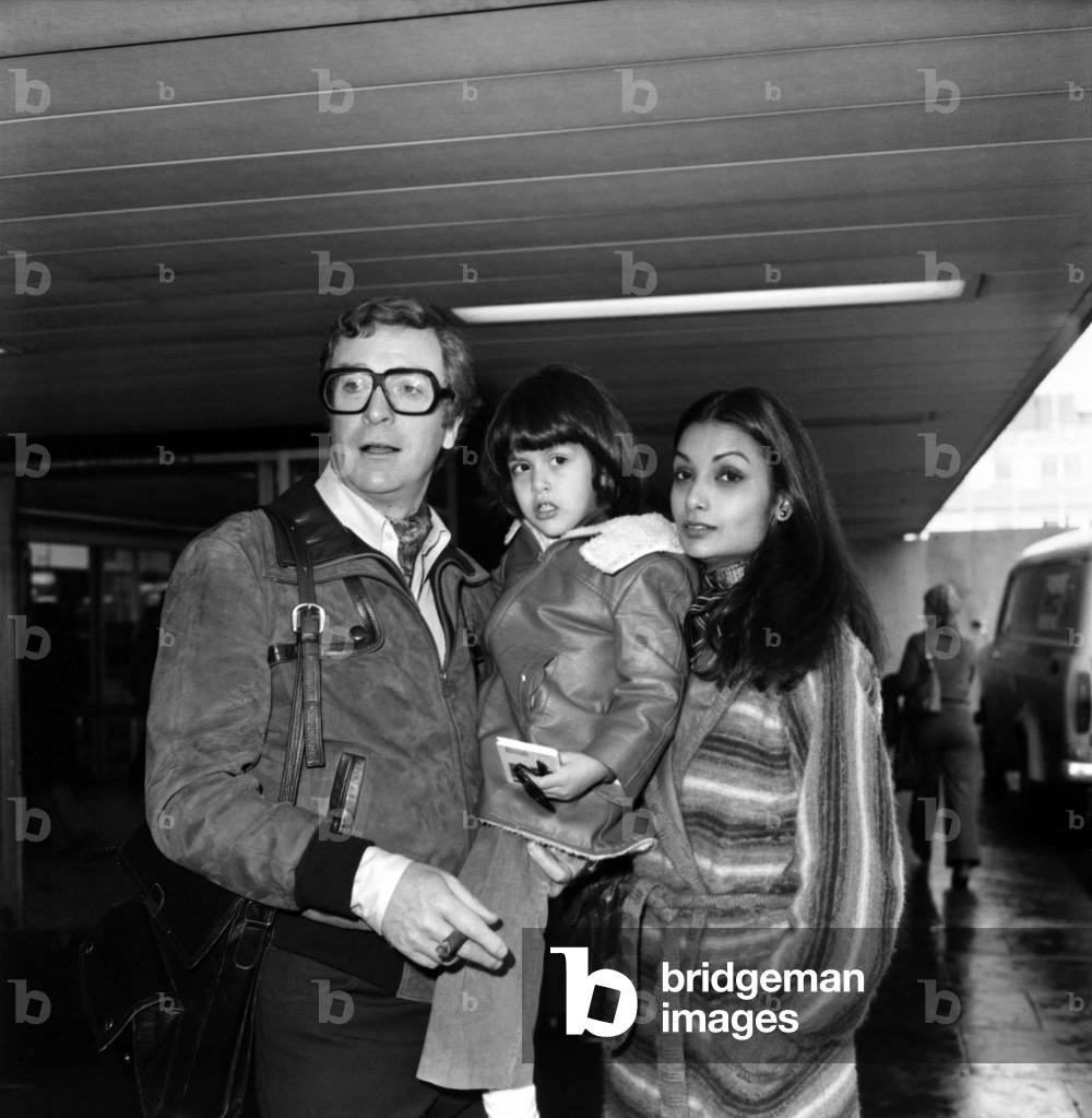 Actor Michael Caine and his wife Shakira leaving London Airport, - seeing them off was his three year old daughter Natasha. Michael and Shakira are off to Las Vegas and Barbados for a months holiday, January 1977 (b/w photo)