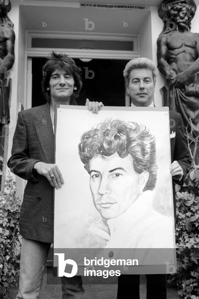 Rolling Stones: Ronnie Wood holds a painting of author Ken Follett who stands next to him. September 1987