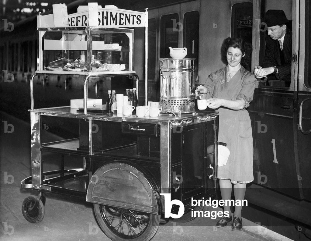 A female worker at Snow Hill Railway station in Birmingham serves a cup of tea from her refreshments trolley to a passenger at the window of his train carriage, introduced by the Western region of British Railways. 31st May 1949 (b/w photo)