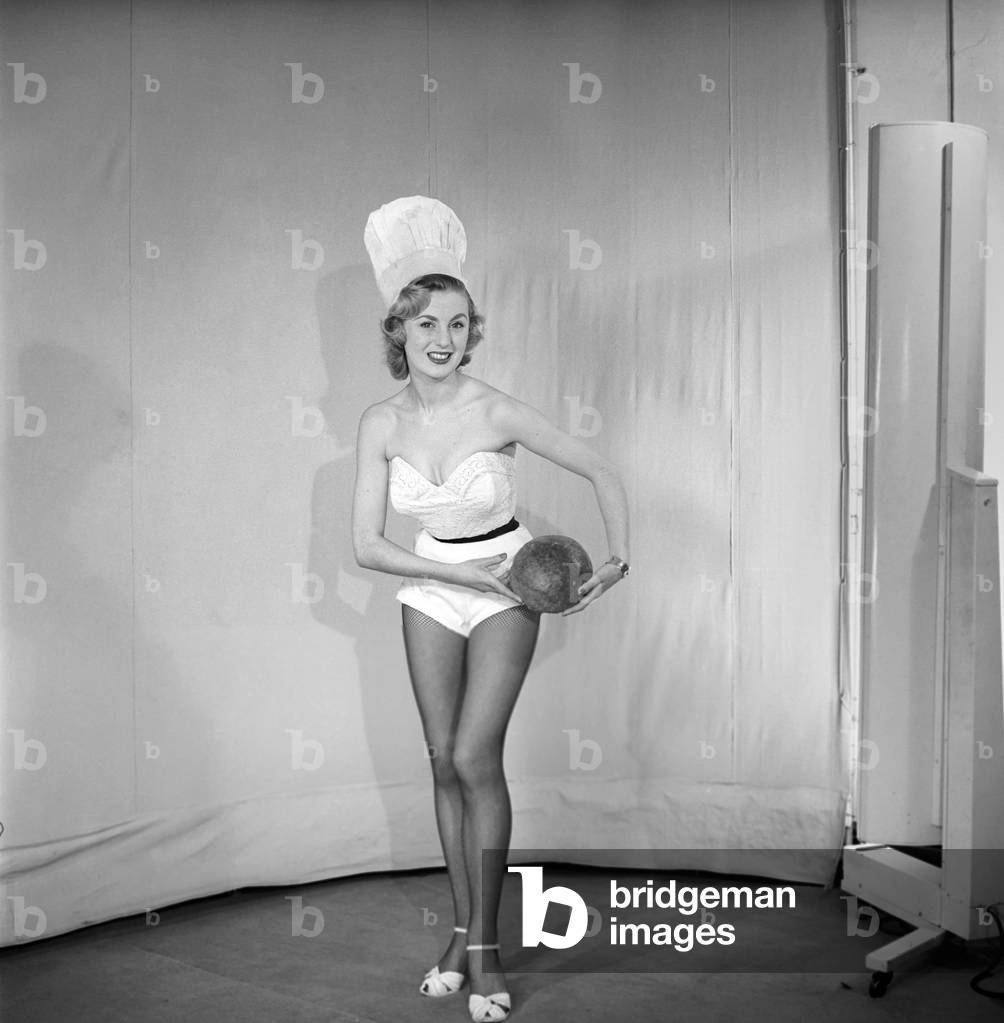 Woman wearing chef's hat holding loaf of bread, April 1959 (b/w photo)