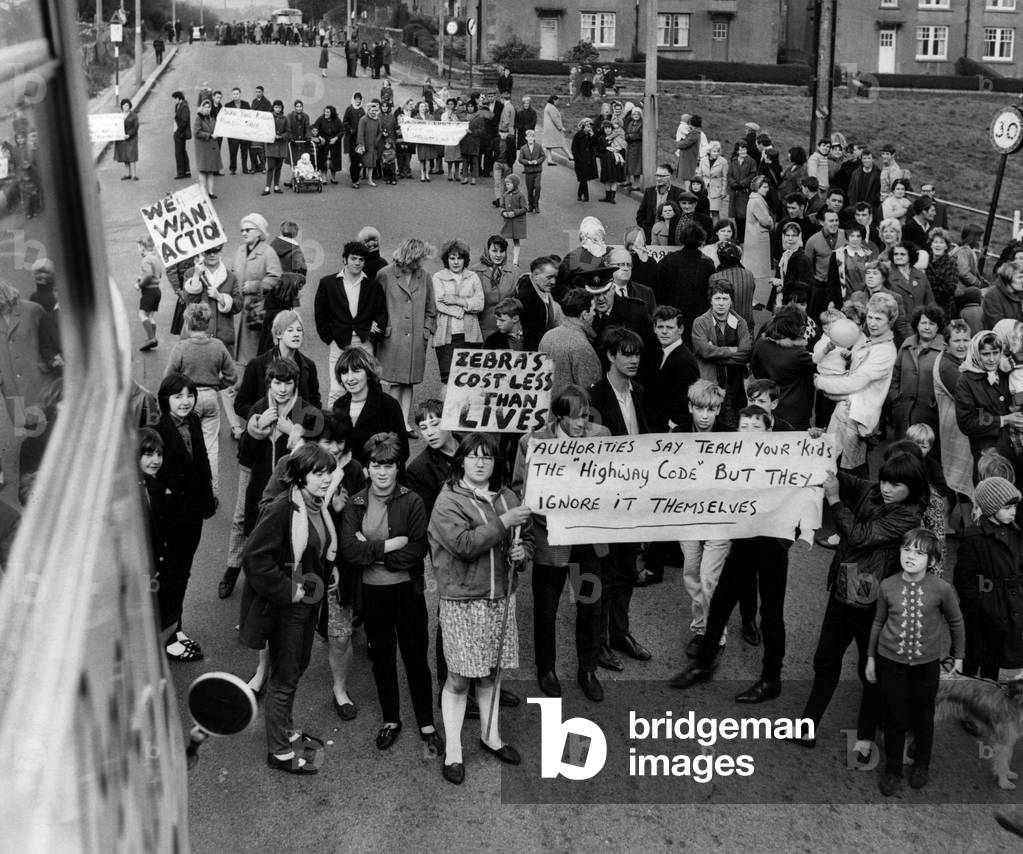 Residents of Tir-Y-Berth stage a demonstration by stopping traffic through the village because they want a 30 m.p.h speed limit introduced. The picture was taken from the top of a double decker bus stopped by the demonstrators, as residents with placards block the road. 19th November 1966 (b/w photo)