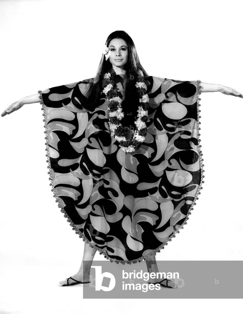 Reveille Fashions: Imogen Woodford. Feminine, floating and butterfly-bright -- this is a wonderful Eastern fashion. Just slip it over the head, and put arms through the wing-sleeves. A garland of flowers gives an extra touch of oriental magic, August 1967 (b/w photo)