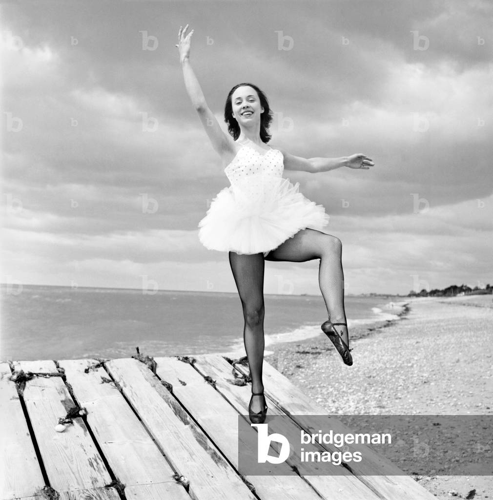 Ballerina Anne Youngmen seen here in a tutu practising her dance moves beside the sea, 1960 (b/w photo)