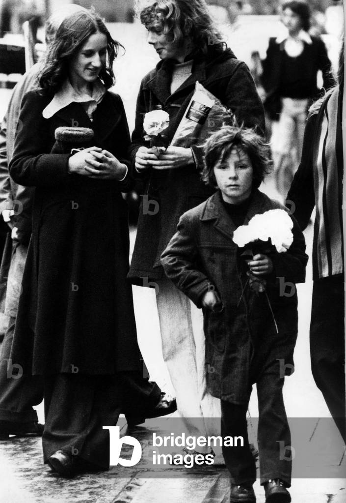 A child selling paper flowers on the streets of Newcastle on 27th December 1974 (b/w photo)