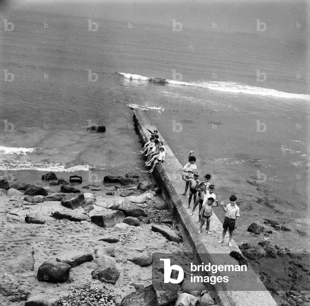 Holidaymakers on a sewerage pipe on the beach at Tynemouth near Newcastle Upon Tyne, Tyne and Wear. June 1960 (b/w photo)