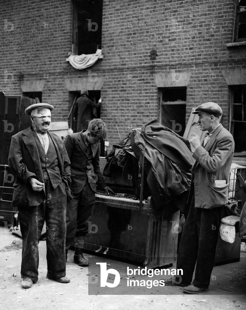 An injured man among his furniture, including a piano following a german doodlebug attack at Deptford. June 1944