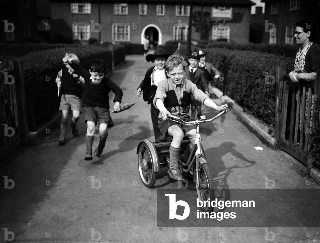 Boys playing on a council estate as one of their mothers looks on, London. 1955 (b/w photo)