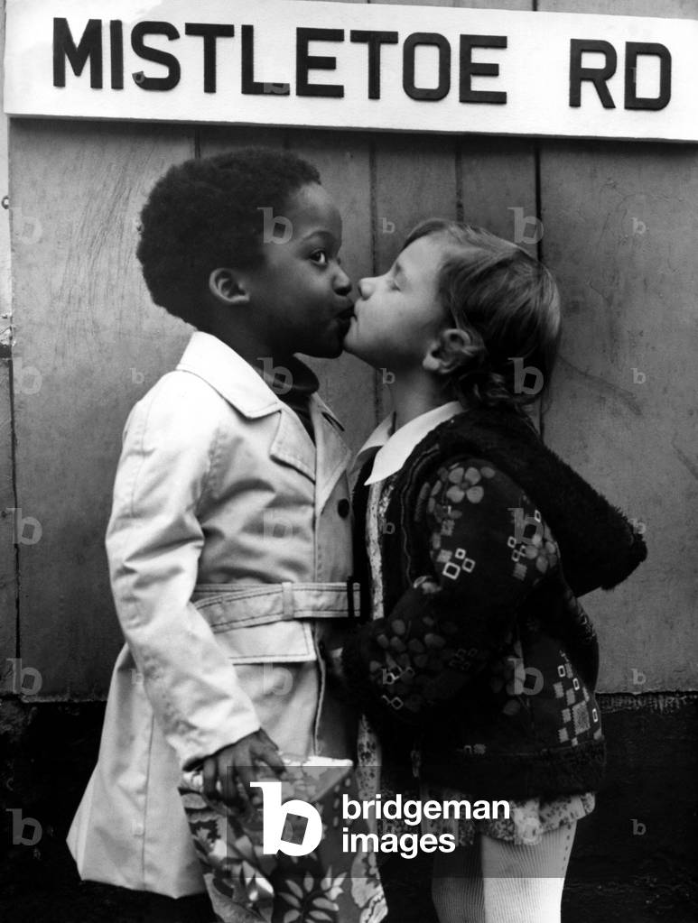 A picture from a series of humurous novelty images taken by Sunday People photographer Dennis Hutchinson - When this Christmas Eve picture was published in the early 1970s it touched the hearts of the region. Two little friends exchange presents and a kiss on Mistletoe Road, Gateshead, c. 1975 (b/w photo)