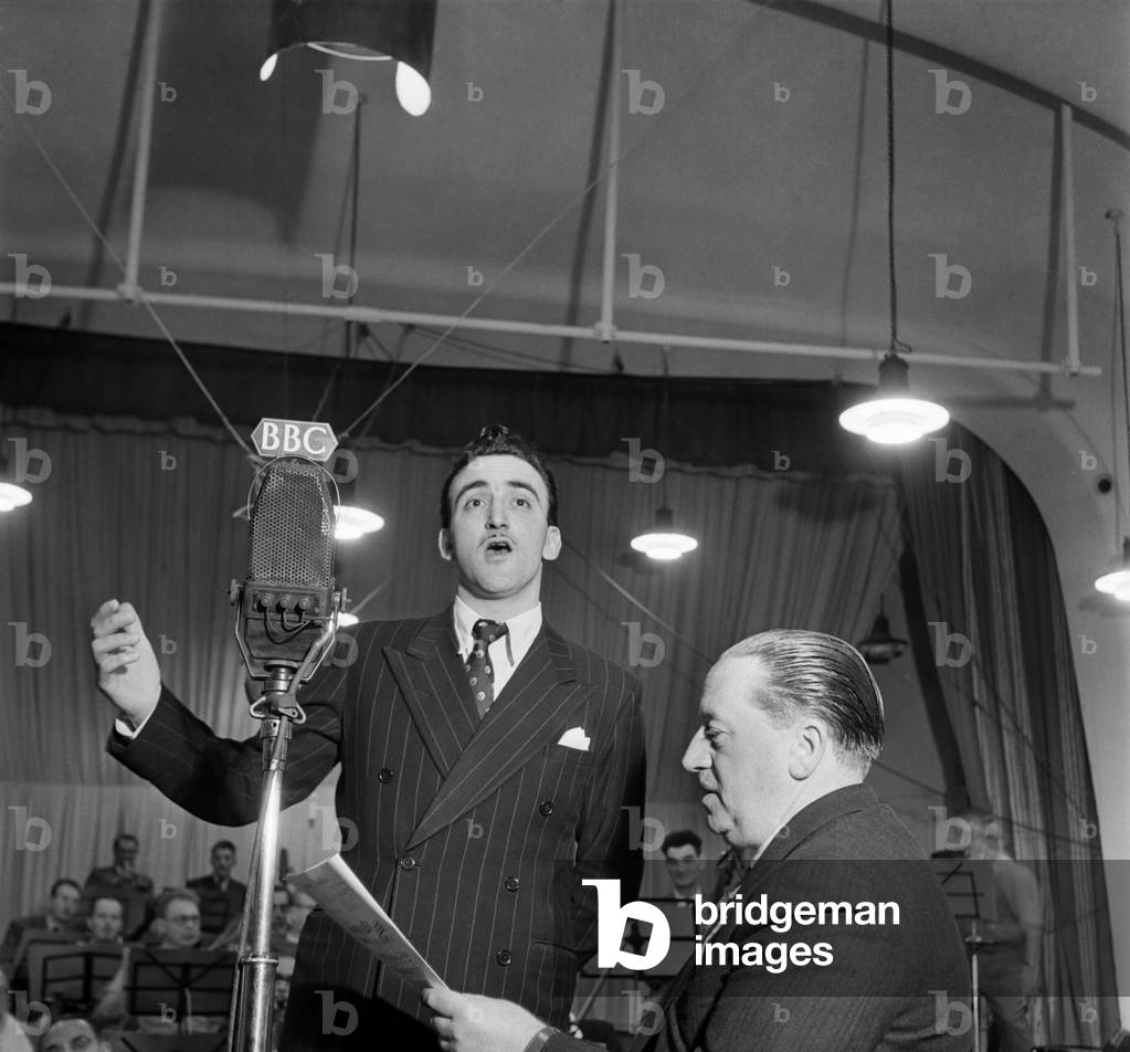 BBC Producer Leslie Bridgemont holds the songsheet for the Singing Waiter as he sings into a BBC microphone. October 1949 O20754-001