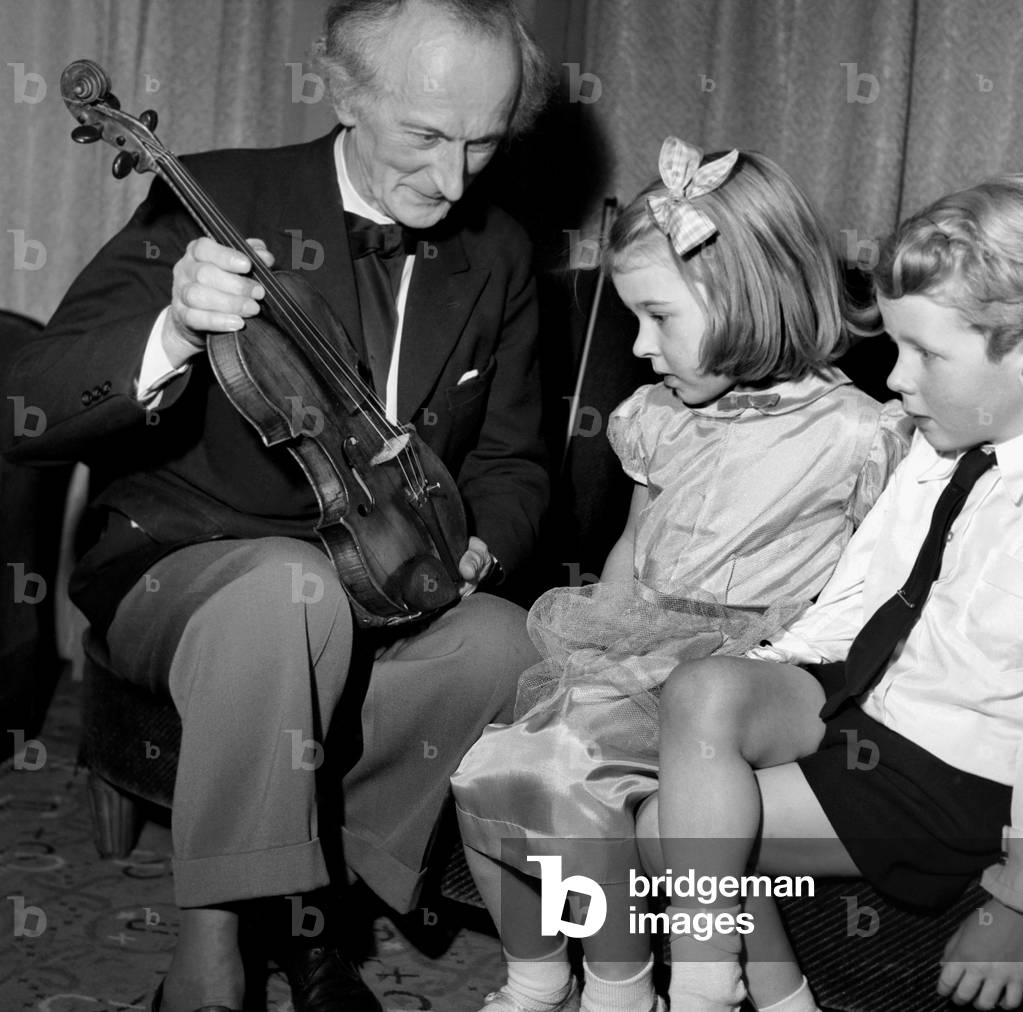 Mr. Plotenjworth, the well known violinist who was performing at the 32nd Actresses Gaiety party at the Dorchester shows John Greenwood Lomox aged 4 of Finchley and Linda Batten, of Twickenham, his 200 year old violin worth over 22,000. T. December 1952 C6429-001