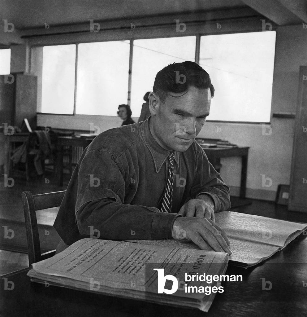 They see with their fingers. His fingers feeling the magic dots, a trainee reads from a Braille copy of World Digest. October 1947 P018623