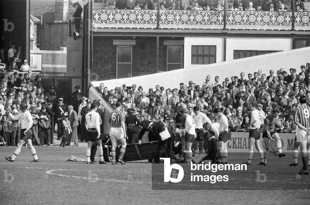 Fulham 1 v. Stoke 1. 1966 League campaignPlayers cluster around George Cohen as ambulance men rush to the scene with a stretcher. 2nd May 1966 (photo)