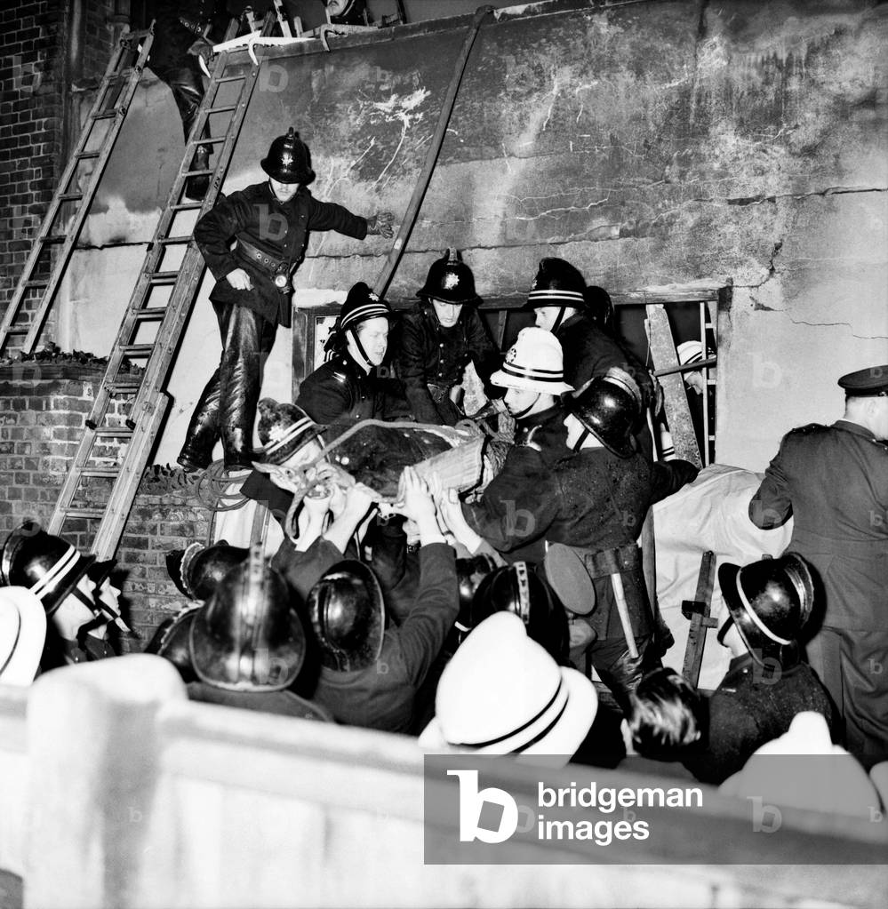 These fireman were trapped, when the roof of an blazing plastics factory in Bond Rd. Melchom, collapsed on them. Fireman helping injured Station Officer John Stacey from thhe blazing factory. December 1969