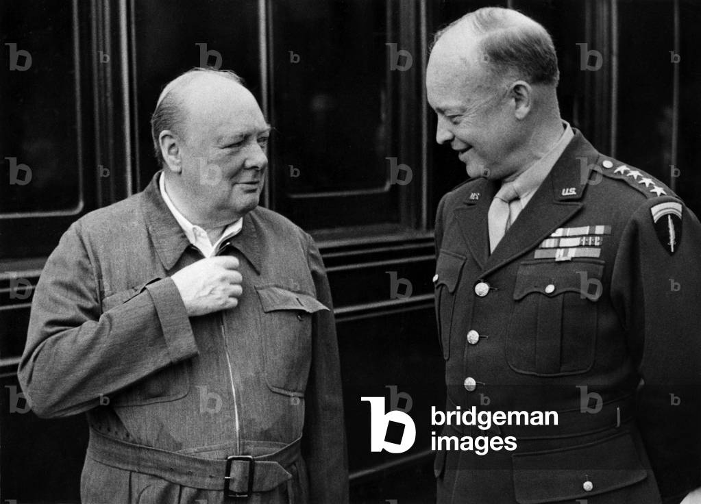 Mr. Churchill demonstrates the zipper on his siren suit to General Eisenhower while strolling along the platform during a halt of the special train in which the party travelled, 15th May, 1944 (b/w photo)