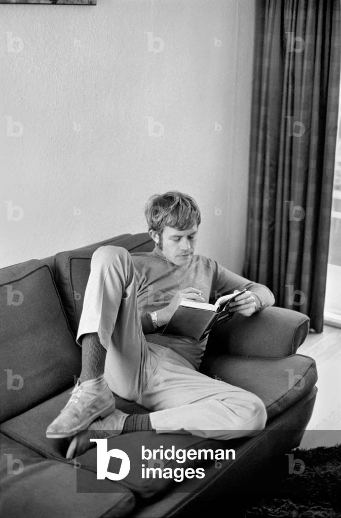 Families: Mother, father and children. Man relaxing at home, reading a book on his sofa, writing at table. November 1969