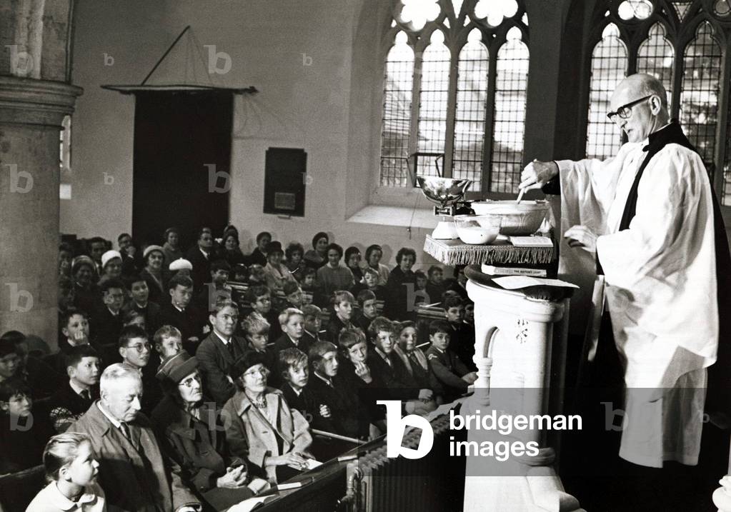 Unusual - A vicar prepares his christmas pudding at a service in church, stirring the mixture in a large mixing bowl. whilst the church goers look on... 25/11/1963