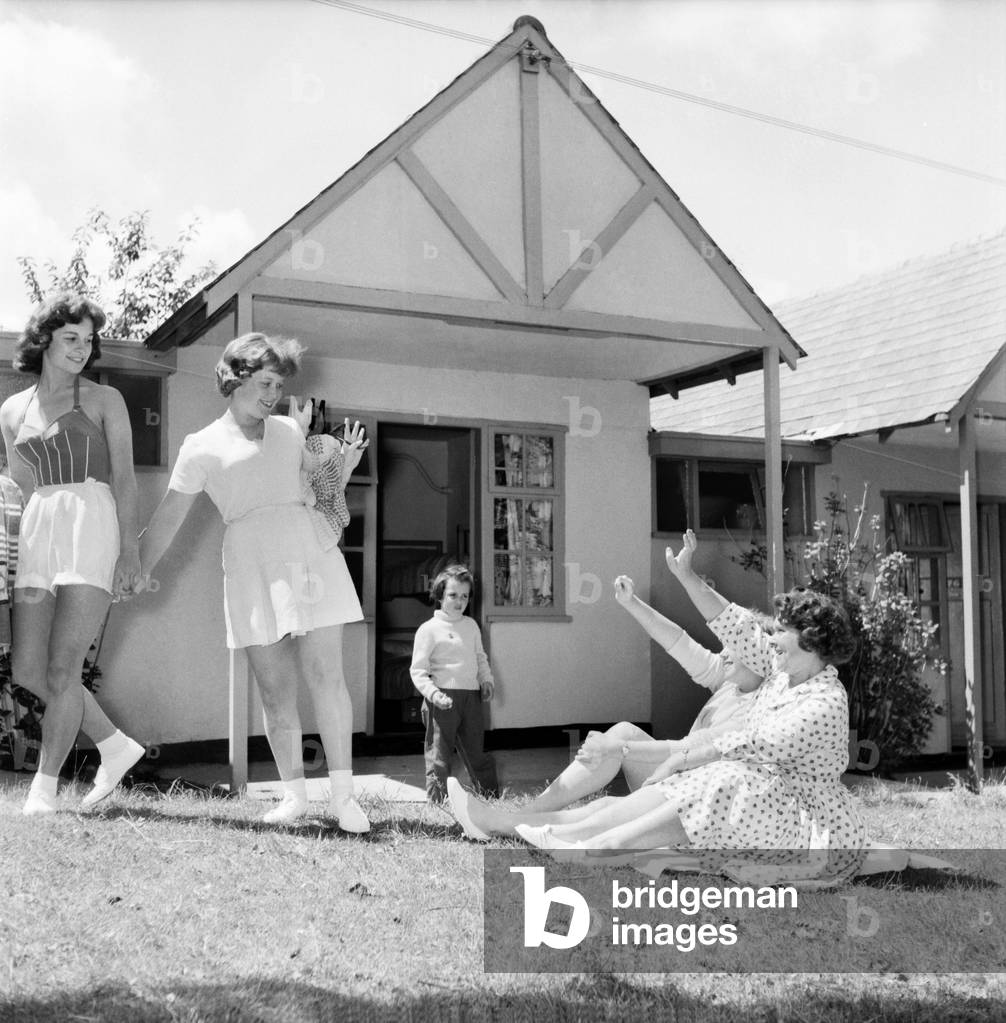 Bultins Holiday Pwllheli: Mrs. Nellie McGrail, Pools Winner. Horse riding/Boating/Elephant/Roller skating/Family. McGrail and Barbara sitting on grass outside their chalet with (standing) Brenda Parsonage (left) and Irene McGrail-both ready to go the swimming pool. June 1960