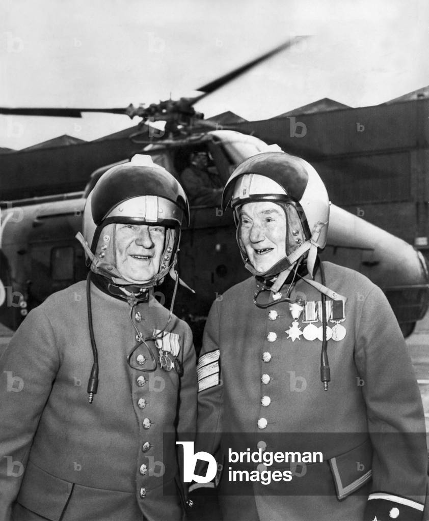 Pensioner Pilots, two helmeted Chelsea Pensioners stand ready for their first helicopter trip. It was a spur-of-the-moment flight for 74-year-old Sapper Charles Lee(right) and Sergeant Richard Oakley, 75(left). August 1963 (b/w photo)