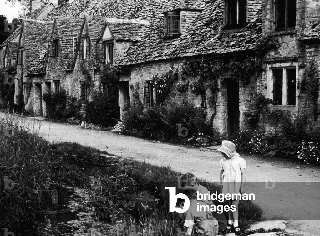 Children playing on the road outside a picturesque row of cottages in Arlington Row in the Cotswold village of Bibury, Gloucestershire, c. 1935 (b/w photo)