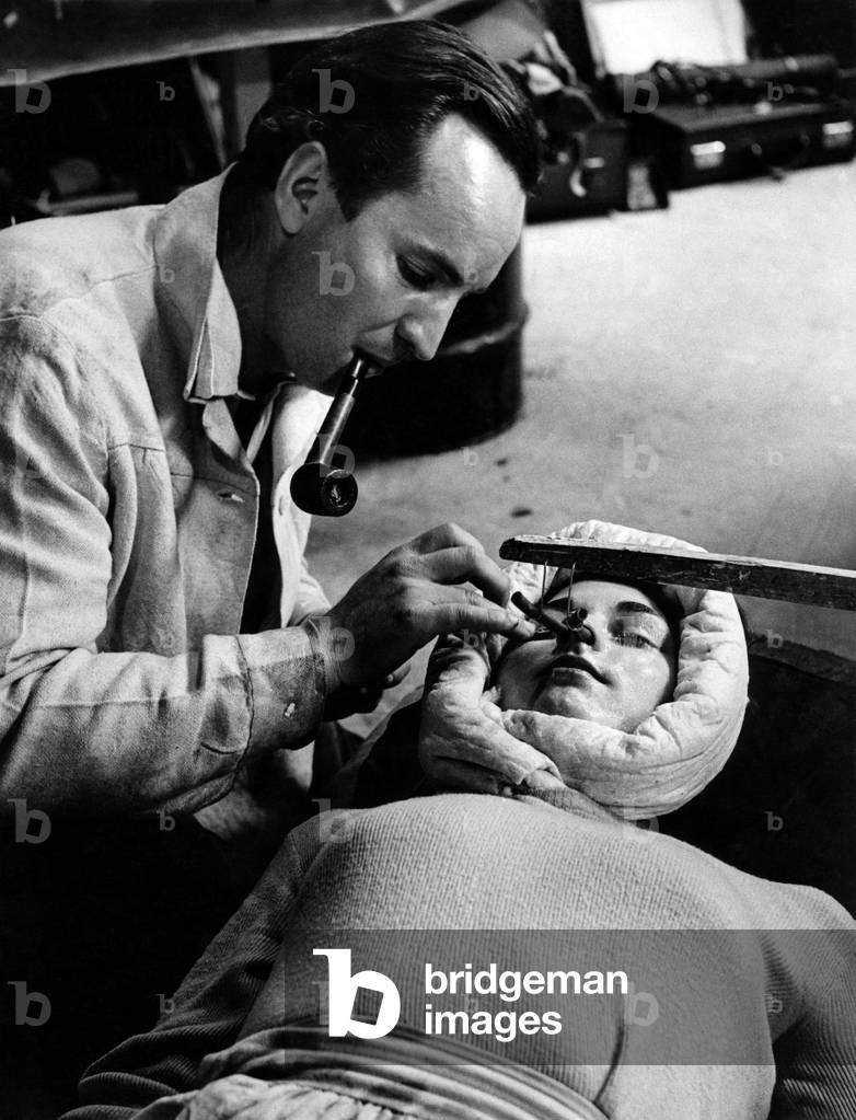 Make up artist John Lee who specialises in creating facial masks is seen here carefully covers the face and eyelids of the actress with vaseline to prevent the plaster sticking and to enable it to come off the face clean when set. June 1947